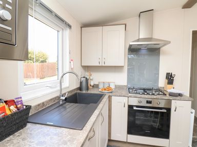 A kitchen with a sink under a window a stove with an oven a kettle and a knife block at Mayflower Lodge in Runswick Bay near Staithes