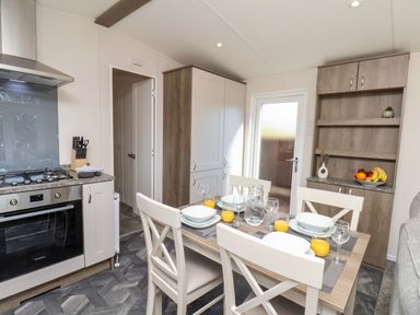 A kitchen dining area with a dining table set for four and a stove and cabinets at Mayflower Lodge in Runswick Bay near Staithes