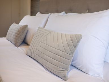 A bed with white pillows and two beige decorative cushions at Mayflower Lodge in Runswick Bay near Staithes