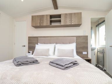 A bedroom with a double bed with pillows and towels and wooden cabinets above the headboard at Mayflower Lodge in Runswick Bay near Staithes