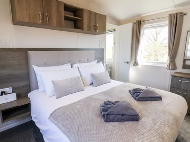 A bedroom with a bed with pillows and folded towels by a window at Mayflower Lodge in Runswick Bay near Staithes