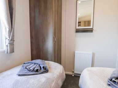 A bedroom with two single beds towels on beds wooden wardrobe mirror and window Mayflower Lodge in Runswick Bay near Staithes