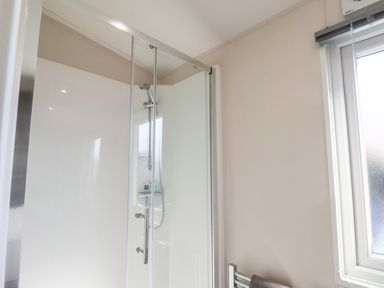 A shower enclosure with glass door and a chrome showerhead next to a window with a towel rail below
