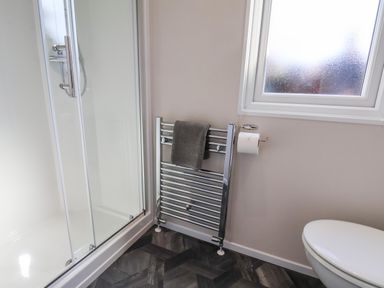 A bathroom with a shower enclosure a towel radiator with a towel a toilet and a frosted window at Mayflower Lodge in Runswick Bay near Staithes