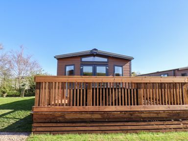 A wooden cabin with a deck and railings on a grassy area at Mayflower Lodge in Runswick Bay near Staithes