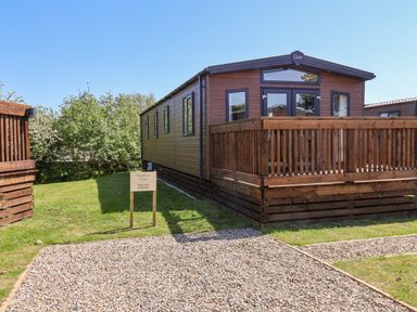A wooden lodge with a deck and gravel parking area surrounded by grass at Mayflower Lodge in Runswick Bay near Staithes