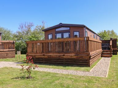 A wooden lodge with a fenced deck and gravel pathway in a grassy area at Mayflower Lodge in Runswick Bay near Staithes