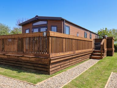 A wooden cabin with a fenced deck and gravel paths on grass at Mayflower Lodge in Runswick Bay near Staithes