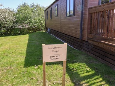 A sign indicating private parking next to a brown wooden building with grass and trees around at Mayflower Lodge in Runswick Bay near Staithes