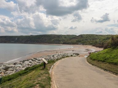 A beach view with people walking along the shore at Mayflower Lodge in Runswick Bay near Staithes