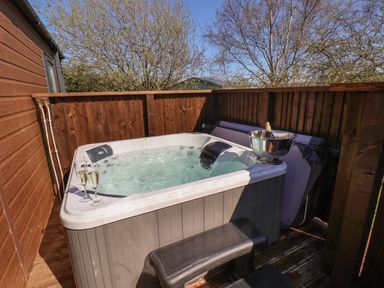 An outdoor hot tub with two glasses of champagne and a bottle in an ice bucket on a fenced wooden deck at Foxglove Lodge Runswick Bay near Staithes