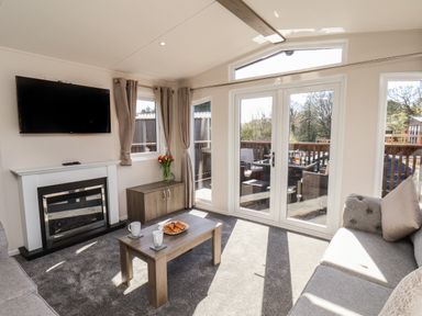 A living room with a fireplace a wall mounted television two sofas a coffee table and glass doors leading to a deck at Foxglove Lodge in Runswick Bay near Staithes