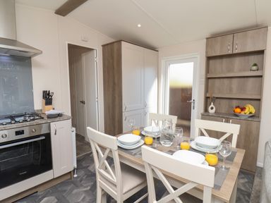 A kitchen with a dining table set with plates and glasses bananas and oranges on a cabinet at Foxglove Lodge in Runswick Bay near Staithes