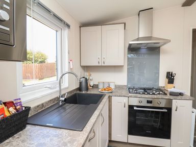 A kitchen with a sink under a window a gas stove oven and cabinets at Foxglove Lodge in Runswick Bay near Staithes