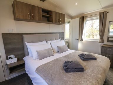 A bedroom with a double bed with pillows and folded towels under a window with curtains at Foxglove Lodge in Runswick Bay near Staithes