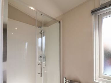 A bathroom shower enclosure with glass door and a window next to it at Foxglove Lodge in Runswick Bay near Staithes