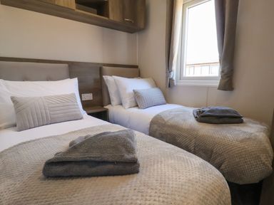 A bedroom with two single beds with pillows and folded towels near a window at Foxglove Lodge in Runswick Bay near Staithes