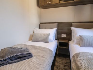A bedroom with two single beds separated by a small bedside table and towels on one bed at Foxglove Lodge in Runswick Bay near Staithes