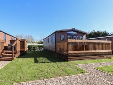 An outdoor view of a wooden lodge with a fenced deck and green grass with gravel paths at Foxglove Lodge in Runswick Bay near Staithes