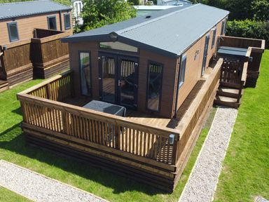 A wooden cabin with a fenced deck and stone path on grass at Foxglove Lodge in Runswick Bay near Staithes