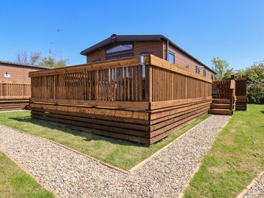A wooden cabin with a raised deck and gravel paths on a grassy area at Foxglove Lodge in Runswick Bay near Staithes