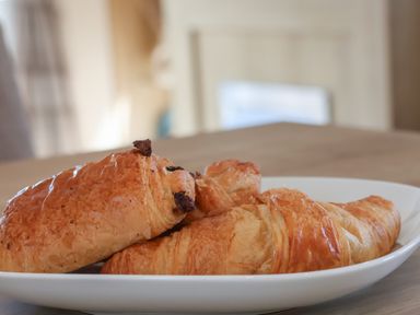 A white plate with a croissant and two pain au chocolat pastries on a wooden table