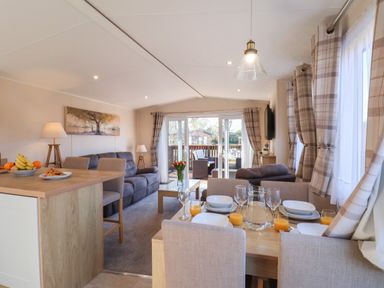A living room and dining area with set table glasses and orange juice at Tulip Lodge in Runswick Bay near Staithes