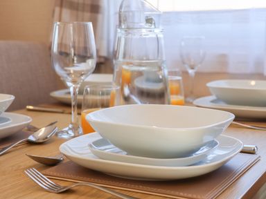 A dining table set with white plates bowls cutlery wine glasses and a water jug at Tulip Lodge Runswick Bay near Staithes