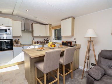 A kitchen with wooden cabinets a countertop with fruit and pastries two bar stools a toaster and a lamp at Tulip Lodge in Runswick Bay near Staithes
