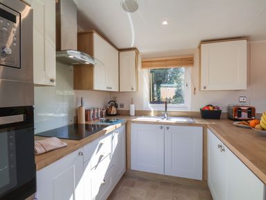 A kitchen with white cabinets wooden countertops a sink a window a stove a microwave and a toaster at Tulip Lodge in Runswick Bay near Staithes