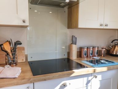 A kitchen countertop with cooking utensils in a holder knives in a wooden block copper canisters a kettle and a glass stovetop at Tulip Lodge in Runswick Bay near Staithes