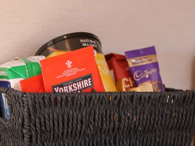 A black woven basket containing packets of Yorkshire tea, a carton of milk, Cadbury hot chocolate, and a container of natural sea salt at Tulip Lodge in Runswick Bay near Staithes