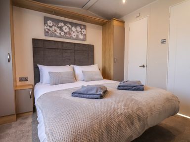 A bedroom with a double bed with folded towels on the bed and floral artwork on the wall at Tulip Lodge in Runswick Bay near Staithes