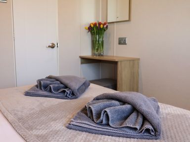 A bedroom with two folded grey towels on a bed and a wooden desk with a vase of tulips at Tulip Lodge in Runswick Bay near Staithes