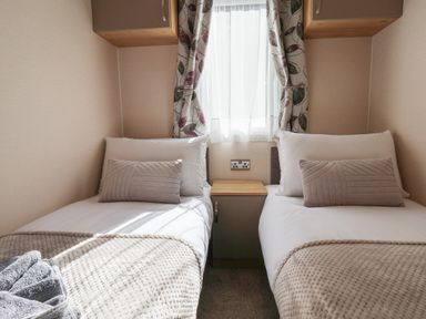 A bedroom with two single beds with pillows and blankets separated by a nightstand under a window at Tulip Lodge in Runswick Bay near Staithes