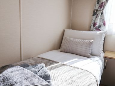 A single bed with pillows and a blanket next to a window with floral curtains at Tulip Lodge in Runswick Bay near Staithes