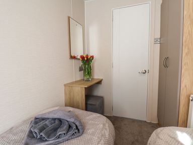 A bedroom with two beds a wooden desk with a vase of flowers a mirror a white door and a wardrobe at Tulip Lodge in Runswick Bay near Staithes