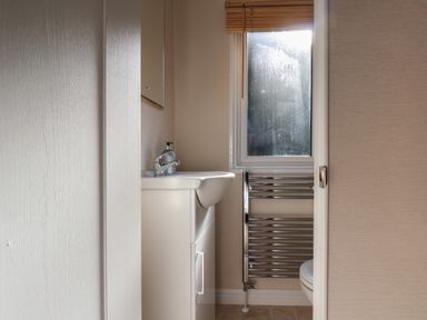 A small bathroom with a white sink cabinet a window with wooden blinds and a chrome towel radiator at Tulip Lodge in Runswick Bay near Staithes