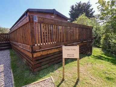 A wooden lodge with a fenced deck and a sign indicating private parking on grass at Tulip Lodge Runswick Bay near Staithes
