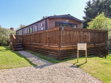 A wooden lodge with a fenced deck and gravel path leading to the entrance at Tulip Lodge in Runswick Bay near Staithes
