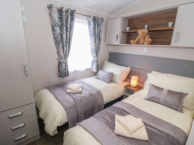 A bedroom with two single beds with purple runners and pillows a teddy bear on a shelf and a small bedside lamp at Buttercup Lodge in Runswick Bay near Staithes