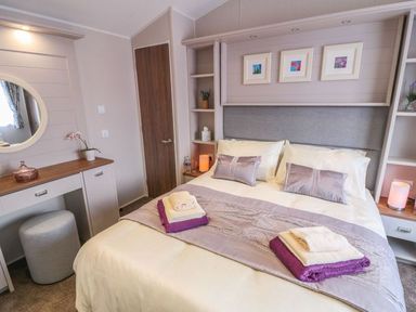 A bedroom with a double bed and folded towels on it a dressing table with a mirror and a stool at Buttercup Lodge in Runswick Bay near Staithes