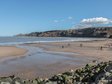 A sandy beach with scattered people and rocky cliffs in the background at Buttercup Lodge in Runswick Bay near Staithes