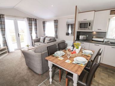 An open living and dining area with a wooden dining table set for four and a grey sofa in the sitting area at Rose Lodge in Runswick Bay near Staithes