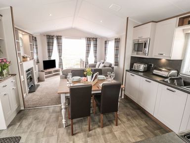 A kitchen and dining area with a table set for four and a living room with sofas and a television at Rose Lodge in Runswick Bay near Staithes