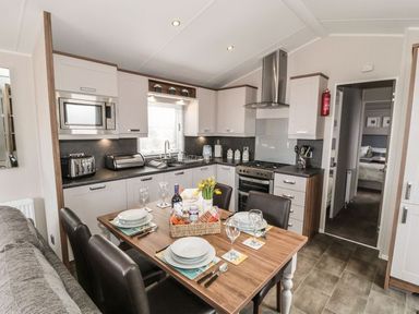 A kitchen with white cabinets a dining table set for four and a doorway leading to a bedroom at Rose Lodge in Runswick Bay near Staithes