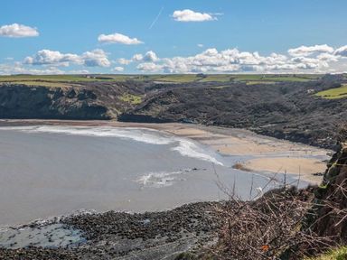 A coastal landscape with a sandy beach and cliffs under a blue sky with clouds at Rose Lodge in Runswick Bay near Staithes