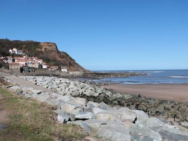 A beach with rocks in the foreground houses on a hill by the coastline at Rose Lodge in Runswick Bay near Staithes
