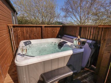 An outdoor hot tub with two glasses of champagne and a bottle in an ice bucket on a wooden deck at Rose Lodge in Runswick Bay near Staithes