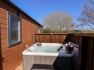 An outdoor hot tub with a glass of champagne and a bottle in a metal bucket on a deck with wooden walls at Rose Lodge in Runswick Bay near Staithes